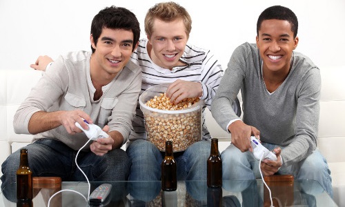 Three friends playing video games while drinking beer and one of them looks slightly sad on the inside. 